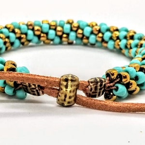 May include: A turquoise and gold beaded bracelet with a brown leather cord and a brass toggle clasp.