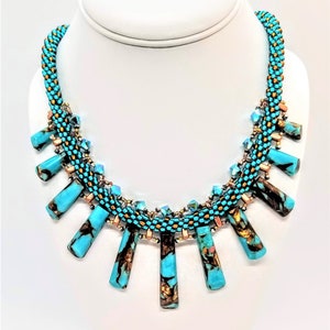 May include: A turquoise and gold beaded necklace with a geometric design. The necklace features a row of turquoise and gold beads with a row of clear crystals on either side. The necklace is finished with a row of turquoise and gold beads that hang down in a fringe.