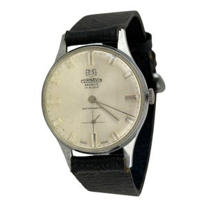 May include: A vintage Cornavin Geneve 17 Rubis wristwatch with a silver-toned case and a black leather band. The watch face is cream-colored with silver hands and markers. The watch is labeled "ANTIMAGNETIC".