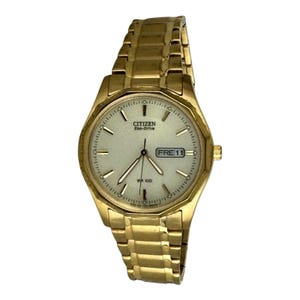 Peut inclure: Montre-bracelet Citizen Eco-Drive dorée avec un cadran clair. La montre affiche la date et possède un bracelet à maillons dorés. Le cadran affiche le texte "CITIZEN Eco-Drive" et "WR 100".