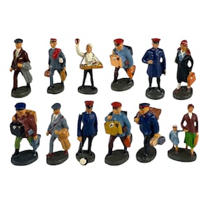 May include: A collection of vintage miniature figurines depicting various figures, including a chef, railway workers, and travelers. The figurines are painted in a variety of colors and carry luggage or other accessories. Each figurine is mounted on a small, oval base.