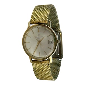 May include: A vintage gold-toned wristwatch with a mesh band. The watch face is silver with gold hands and markers, and a date window at the 3 o'clock position. The watch is marked "ETERNA-MATIC 3000".