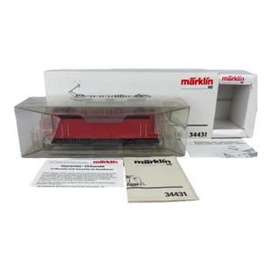 May include: A red Märklin HO model train locomotive in a clear plastic case, with the box and paperwork visible. The box is white with the Märklin logo and the number 34431. The model train is a detailed replica.