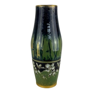 Op de afbeelding: Een decoratieve vaas met een geschilderde bosscène. De vaas heeft een donkerblauwe bovenkant met gouden details, overgaand in een groen en zwart lichaam met witte bloemmotieven. De basis is ook goudkleurig, ongeveer 25 cm hoog.