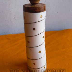May include: A decorative bottle stopper with a wooden top and base, and a white body adorned with gold-coloured dots and a spiral design. The text "THE KNIGHT ARMOURY" is at the bottom.