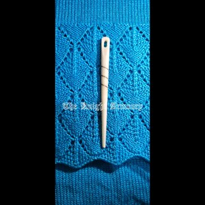 May include: A cream-coloured knitting needle with a spiral design, on blue knitted fabric with a diamond pattern. The text "The Knight Armoury" is visible on the fabric.