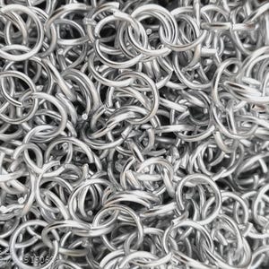 May include: Close-up of a pile of silver-colored metal rings, tightly interlocked. The rings are uniform in size and shape, creating a dense, textured surface. The metal has a shiny, reflective quality, suggesting a polished finish. The image conveys a sense of industrial or craft materials.