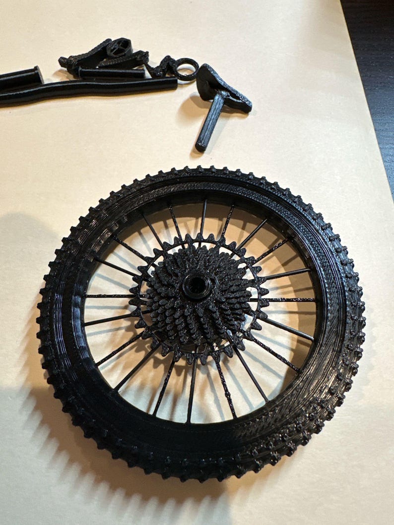 May include: A black bicycle wheel with a detailed spoke and gear design. The tire has a textured surface. Additional black bicycle parts are scattered around the wheel, including a seat and other components.