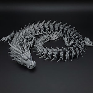 May include: A grey, articulated dragon figurine with a detailed, spiky design. The dragon is posed in a curved position, with its head and tail visible. The figurine is made of a solid material and has a matte finish.