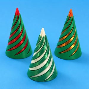 Peut inclure: Trois décorations de sapin de Noël. Les arbres sont verts avec des accents rouges, dorés et blancs. Les ornements sont en forme de cône avec un motif en spirale et reposent sur une surface bleue.