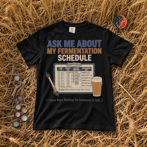 Könnte beinhalten: Ein schwarzes T-Shirt mit dem Text "ASK ME ABOUT MY FERMENTATION SCHEDULE" in Blau und Beige. Darunter befindet sich eine Grafik eines Klemmbretts mit Braudaten, einem Aräometer und einem Bierglas sowie der Text "( I Have Been Waiting for Someone to Ask. )".