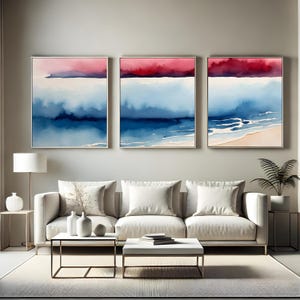 Peut inclure: Trois peintures à l'aquarelle encadrées représentant un paysage marin abstrait. Chaque œuvre présente un dégradé de couleurs, avec un ciel rouge et rose, un océan bleu et une plage de sable dans une peinture. L'œuvre est exposée au-dessus d'un canapé blanc.