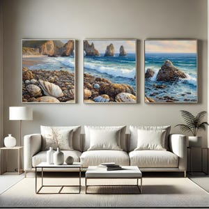 Puede incluir: Tres pinturas de paisajes enmarcadas que representan escenas costeras con olas del océano, rocas y acantilados. La obra de arte presenta una paleta de colores neutros con tonos de azul, marrón y beige. Las pinturas se exhiben sobre un sofá blanco.