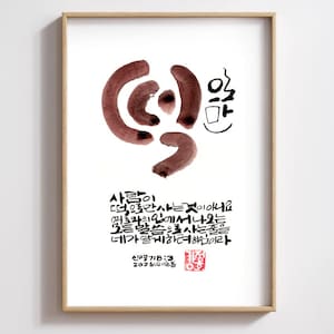 Op de afbeelding: Een ingelijste kunstdruk met Koreaanse kalligrafie in bruine en zwarte inkt op een witte achtergrond. Het kunstwerk bevat abstracte vormen en tekst. De lijst is gemaakt van lichtgekleurd hout.