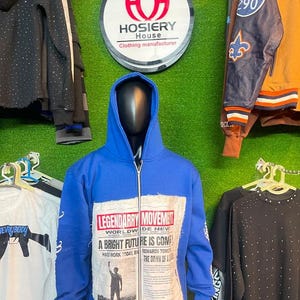 Peut inclure: Un sweat à capuche bleu vif zippé avec un grand écusson rectangulaire sur le devant portant le texte LEGENDARRY MOVEMENT, A BRIGHT FUTURE IS COMING, et d'autres phrases imprimées à côté d'une silhouette d'une personne levant le bras.