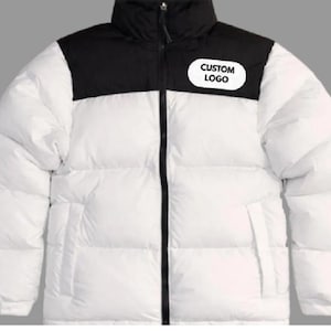 May include: A white and black puffer jacket with a high collar and a full-length zipper. The jacket has a black upper yoke and a white body. A white oval patch with the text "CUSTOM LOGO" is on the upper left chest.