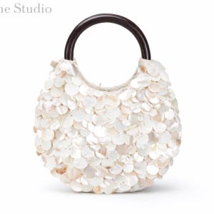 Peut inclure: Un sac à main rond recouvert de disques de coquillages blancs irisés superposés, doté d'une poignée circulaire marron foncé. Le sac présente une silhouette incurvée et structurée avec une texture dense et stratifiée sur l'extérieur.