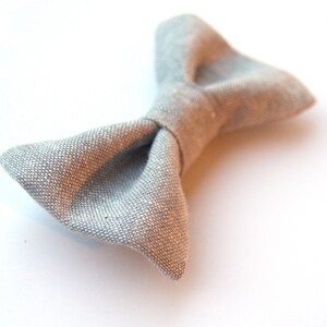 May include: A gray linen bow tie. The bow tie is made of a soft, textured fabric.