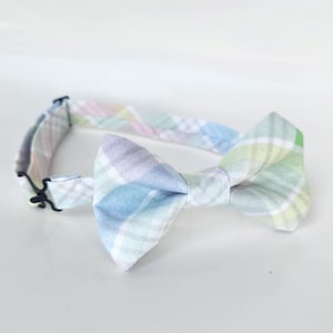 May include: A pastel plaid bow tie with a light blue, green, pink, and white pattern. The bow tie is made of fabric and has a black adjustable strap.