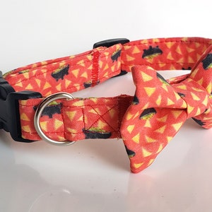 May include: A red dog collar with a black buckle and a matching bow tie. The collar and bow tie feature a pattern of yellow triangles and black bowls with green guacamole.