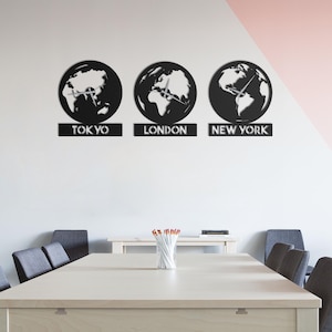 May include: A black metal wall clock set featuring three globes, each with clock hands. The clocks are labeled "TOKYO", "LONDON", and "NEW YORK". The clocks are mounted on a white wall.