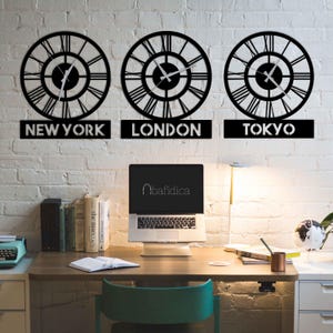 May include: Three black metal wall clocks with Roman numerals, each labeled with a city: New York, London, and Tokyo. The clocks are mounted on a white brick wall above a desk with a laptop and books.