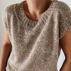 May include: A beige knit top with a scoop neckline and short sleeves. The top has a speckled pattern and a textured appearance. The knitwear is a neutral color, suitable for various outfits.