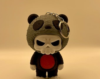 May include: A 3D-printed keychain featuring a panda-skull character. The figure has a gray panda hood with black ears, a skull-shaped face, and a red circular detail on the chest. The keychain is attached to a silver ring.