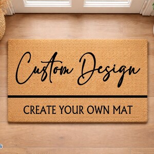 May include: A rectangular doormat with the words "Custom Design" in a stylish script above a black horizontal line. Below the line, the text reads "CREATE YOUR OWN MAT" in a sans-serif font. The mat is a light brown color.