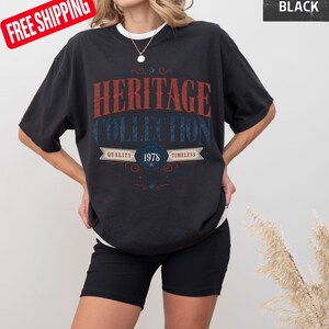 May include: Black t-shirt with the text "HERITAGE COLLECTION" in red and blue. The shirt also features the text "QUALITY 1978 TIMELESS". The shirt is worn with black shorts.