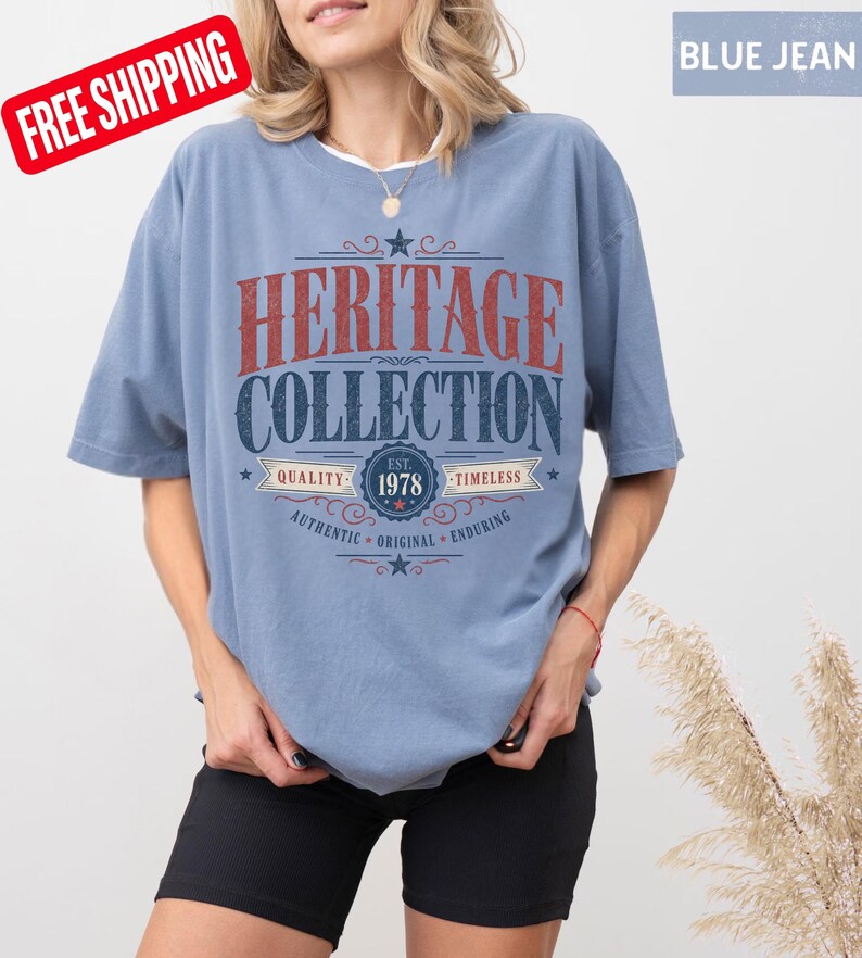 May include: A pale blue t-shirt with the words "HERITAGE COLLECTION" in red and navy blue. The shirt also features the text "EST. 1978" and the words "QUALITY", "TIMELESS", "AUTHENTIC", "ORIGINAL", and "ENDURING".