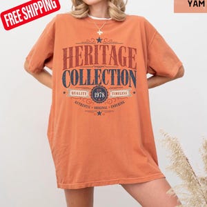 May include: An orange t-shirt featuring the text "HERITAGE COLLECTION" in a retro design. The shirt includes the year "1978" and the words "Quality, Timeless, Authentic, Original, Enduring". The t-shirt is a solid colour.