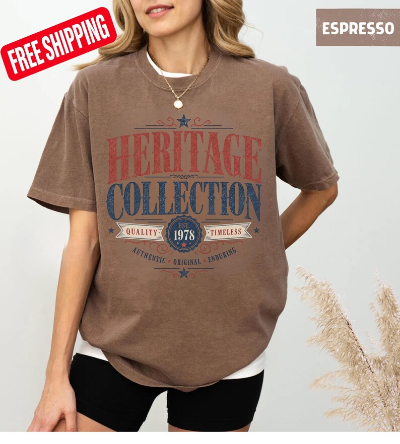 May include: Brown t-shirt with the text "HERITAGE COLLECTION" in red and blue. The shirt also features the text "EST. 1978" and the words "QUALITY", "TIMELESS", "AUTHENTIC", "ORIGINAL", and "ENDURING". The shirt is a solid brown colour.