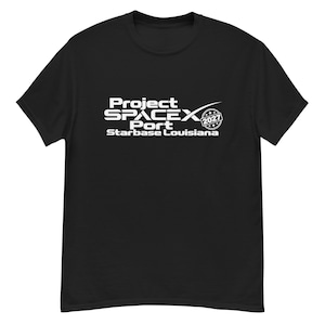 May include: A black short-sleeved t-shirt featuring white text that reads Project SPACEX Port Starbase Louisiana with a circular emblem containing the year 2027. The design is centred on the chest of the shirt, which has a crew neckline.