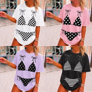 May include: Four t-shirts, each featuring a bikini design. The designs include a black and white checkered pattern, black polka dots, black hearts, and black and white stripes. The shirts are white, pink, lavender, and black.