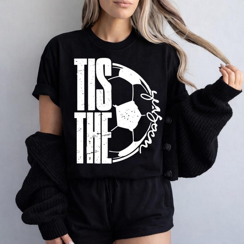 Peut inclure: T-shirt noir avec le texte "TIS THE SEASON" en lettres blanches et un graphisme de ballon de football blanc. Le mot "season" est &eacute;crit en cursive. Le t-shirt est &agrave; manches courtes.