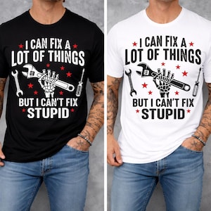 May include: Black and white t-shirts with the text "I CAN FIX A LOT OF THINGS BUT I CAN'T FIX STUPID". The design includes a wrench, screwdriver, and a skeleton hand holding a wrench, with red star accents.