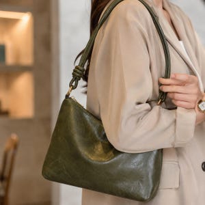 Pu&ograve; includere: Borsa a tracolla in pelle verde oliva con cerniera dorata e cinturino verde abbinato. La borsa ha un design elegante e minimalista, perfetta per l'uso quotidiano. La borsa &egrave; realizzata in pelle morbida e strutturata.