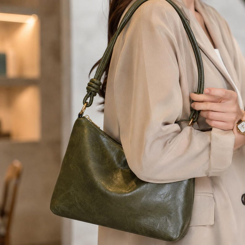 Pu&ograve; includere: Borsa a tracolla in pelle verde oliva con cerniera dorata e cinturino verde abbinato. La borsa ha un design elegante e minimalista, perfetta per l'uso quotidiano. La borsa &egrave; realizzata in pelle morbida e strutturata.