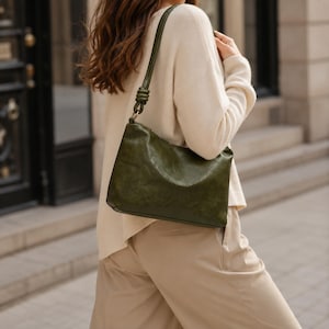 Pu&ograve; includere: Borsa a tracolla verde oliva con dettaglio a nodo sulla tracolla. La borsa ha una forma rettangolare e un aspetto in pelle leggermente invecchiata. La tracolla &egrave; sottile.