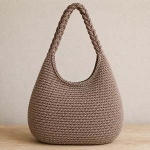 May include: A taupe-colored hobo bag crafted from a dense, uniform crochet stitch. The bag features a rounded, teardrop-shaped body and a single, thick handle with a prominent braided texture that seamlessly integrates into the top of the bag.