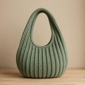 May include: A sage green crochet handbag featuring a rounded, hobo-style silhouette with a prominent vertical ribbed texture. The bag is constructed with a single integrated handle and a wide, curved opening, showcasing a consistent yarn stitch pattern.