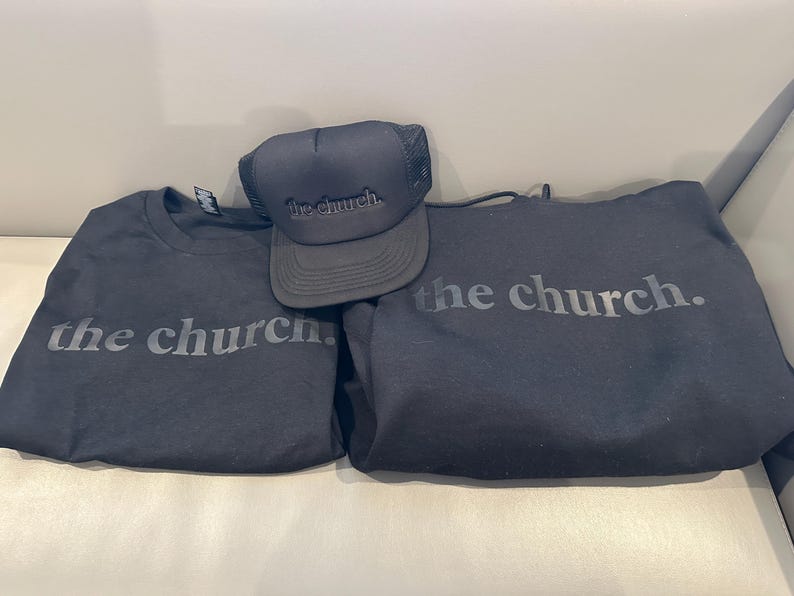 May include: Black apparel set featuring the text "the church." Includes a black crew neck t-shirt, a black hoodie, and a black trucker hat. The hat has a mesh back and the text is in a tone-on-tone design.
