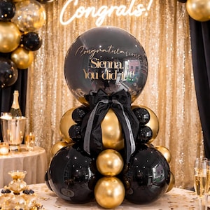 Puede incluir: Un arreglo de globos en negro y dorado. Un gran globo negro muestra el texto "Congratulations Sienna, You did it!!!". En el fondo, un letrero de neón "Congrats!" y tela de lentejuelas doradas.