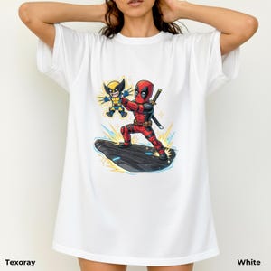 Puede incluir: Camiseta blanca con un gr&aacute;fico colorido de Deadpool y Wolverine. Deadpool viste un traje rojo y negro, empu&ntilde;ando una espada, y Wolverine un traje amarillo y azul. El texto "Texoray" est&aacute; abajo a la izquierda y "White" abajo a la derecha.