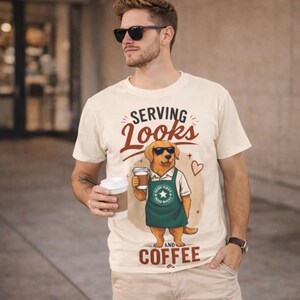 Könnte beinhalten: Cremefarbenes T-Shirt mit der Aufschrift "SERVING LOOKS AND COFFEE" und einem Cartoon-Hund mit Sonnenbrille und Schürze. Der Hund hält eine Kaffeetasse. Die Person im Bild trägt eine Sonnenbrille und eine khakifarbene Hose.