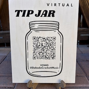 May include: A wooden sign with the words "TIP JAR" and "VIRTUAL" in black. A black line drawing of a mason jar with a QR code is in the center. The Venmo handle @DakodaCrockettMusic is below the jar.