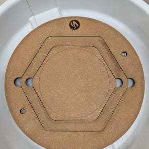 May include: A brown wooden pottery wheel bat with a circular design and a central hexagon shape. The bat has a logo in the upper center and is set inside a white plastic basin. Two screws secure the bat to the basin.
