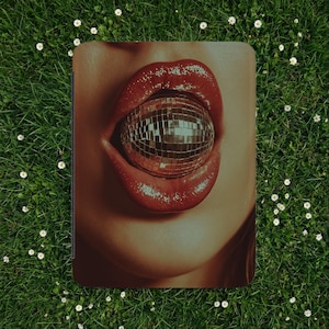 May include: A rectangular tablet or e-reader case featuring a graphic print of a pair of glossy red lips holding a reflective, multi-faceted silver disco ball between them. The design covers the entire front surface of the protective cover.
