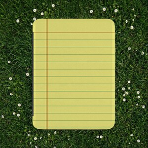 Puede incluir: Un bloc de notas amarillo con líneas verdes horizontales y una línea de margen roja vertical. El bloc de notas está sobre un fondo de hierba verde y pequeñas flores blancas.